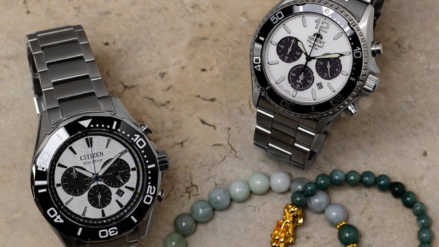 The Citizen Endeavor Chrono and the Orient TX02 Solar Chronograph on steel bracelets, resting on stone beside jade bead bracelets